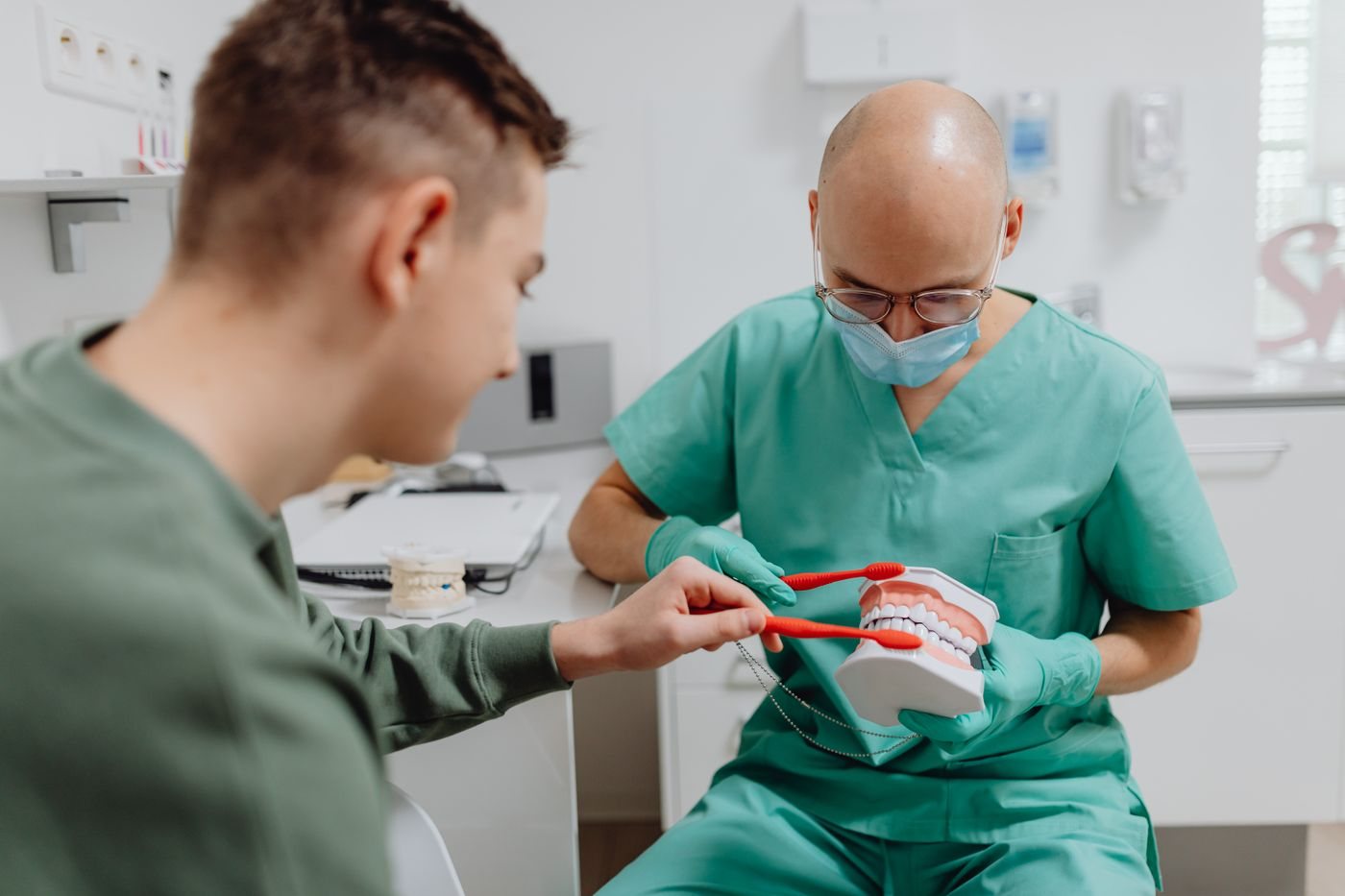 A dental professional showing a young patient how to brush, using a model of the teeth.